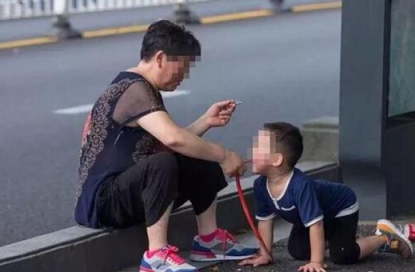 大妈坐街头一边抽烟 一边让孙子学狗爬嘴还叼玩具蛇